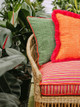 Wooden chair in greenhouse with plants showcasing peace and love outdoor seat cushion with Bulu outdoor Arancio and Prato cushions. Photography by Christopher Horwood
